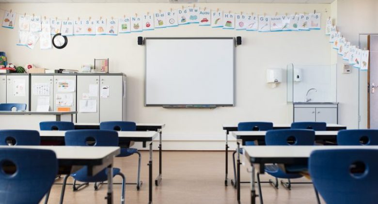 School desk and chairs in empty modern classroom. Empty class room with white board and projector in elementary school. Primary classroom with smartboard and alphabet on wall.